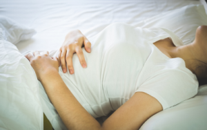 woman lying on a bed in pain holding her tummy